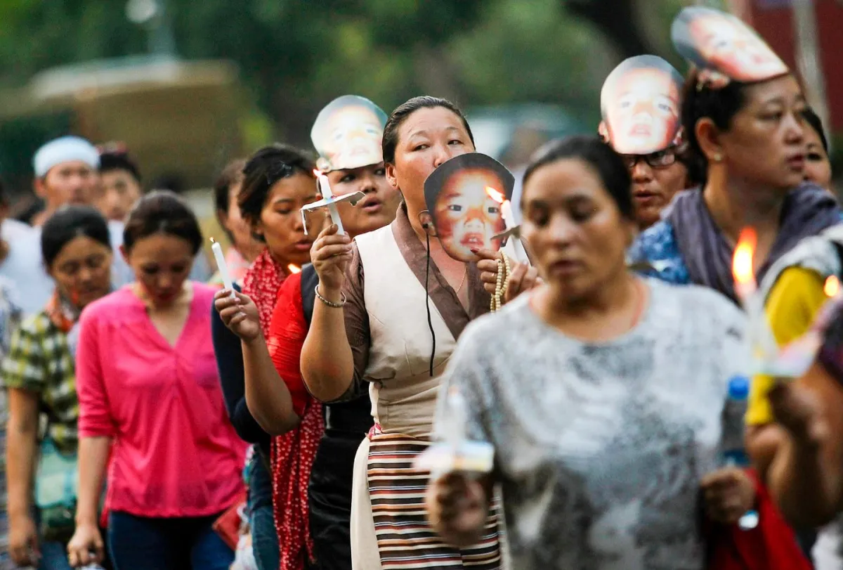 Tibetan exiles hold candles and wear masks of Gedhun Choekyi Nyima