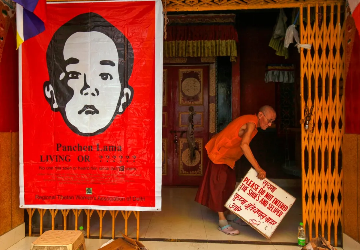 A Tibetan monk holds a sign board next to a poster of Gedhun Choekyi Nyima